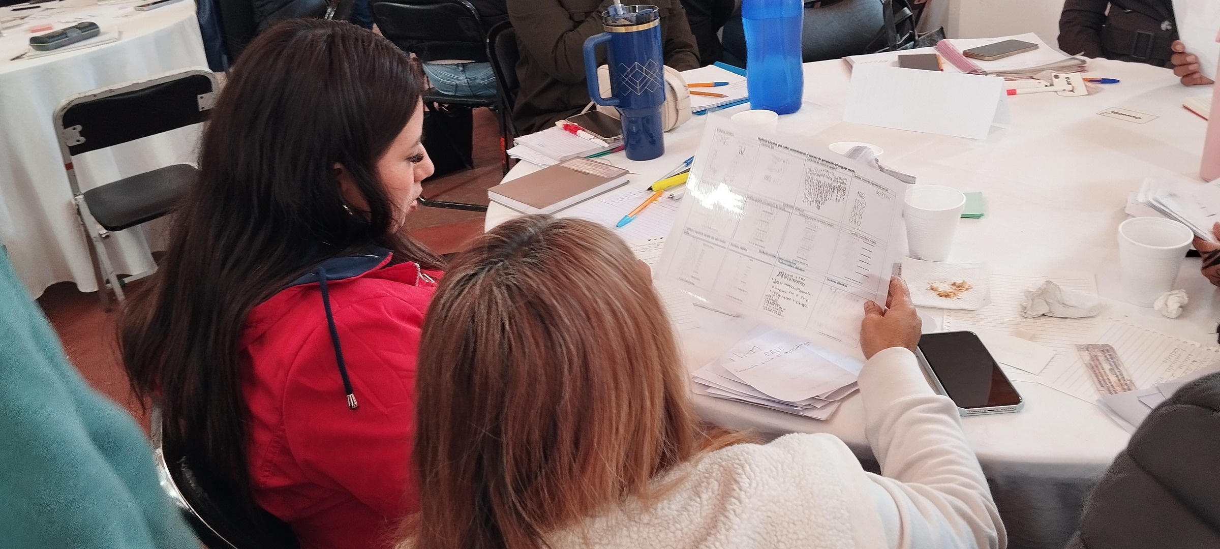 Personas conversan alrededor de una mesa con materiales de trabajo.
