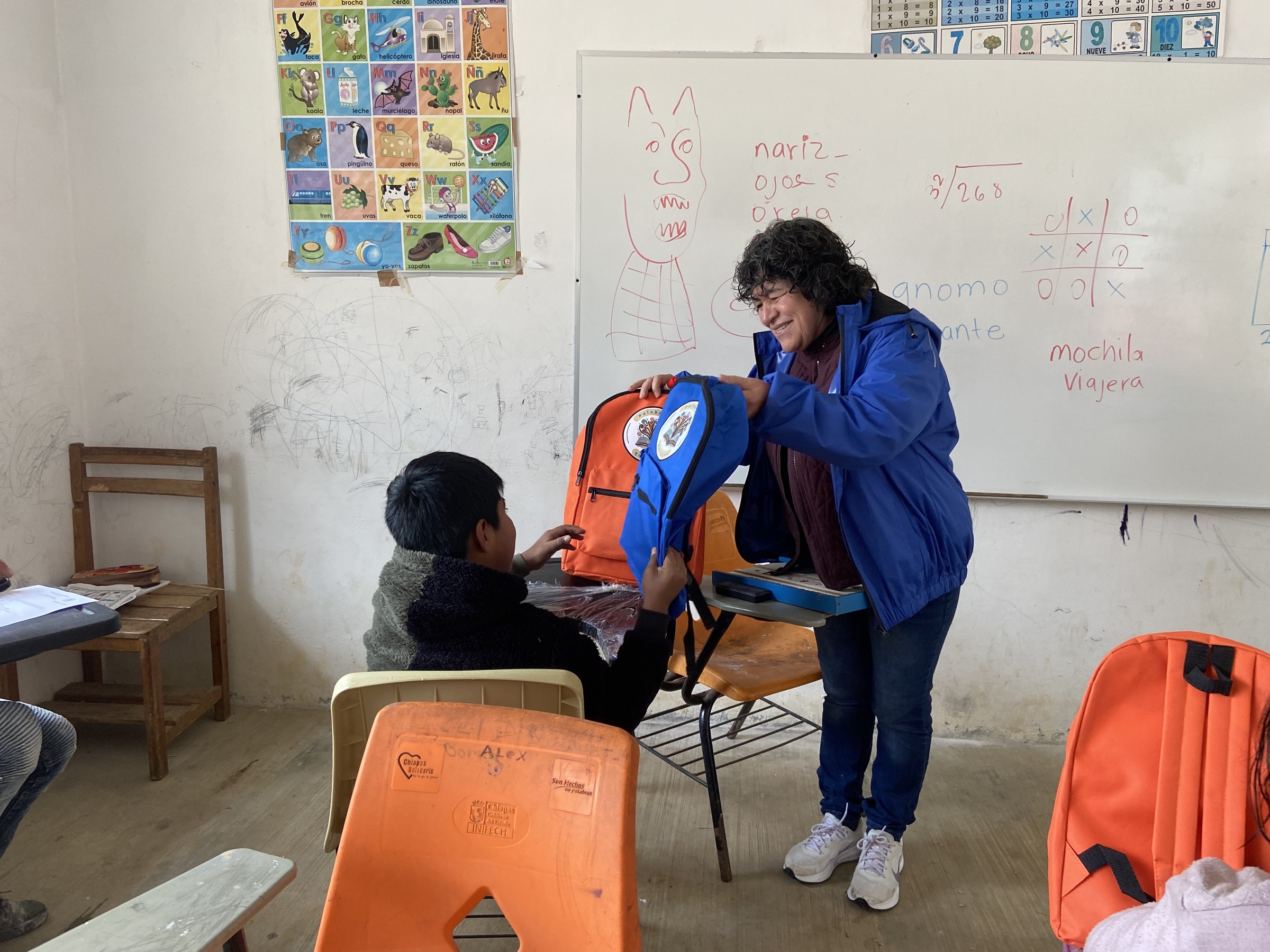 Una persona entrega una mochila a otra en un aula.